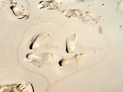 Honeymooners leave a heart with their names and footprints in the sand